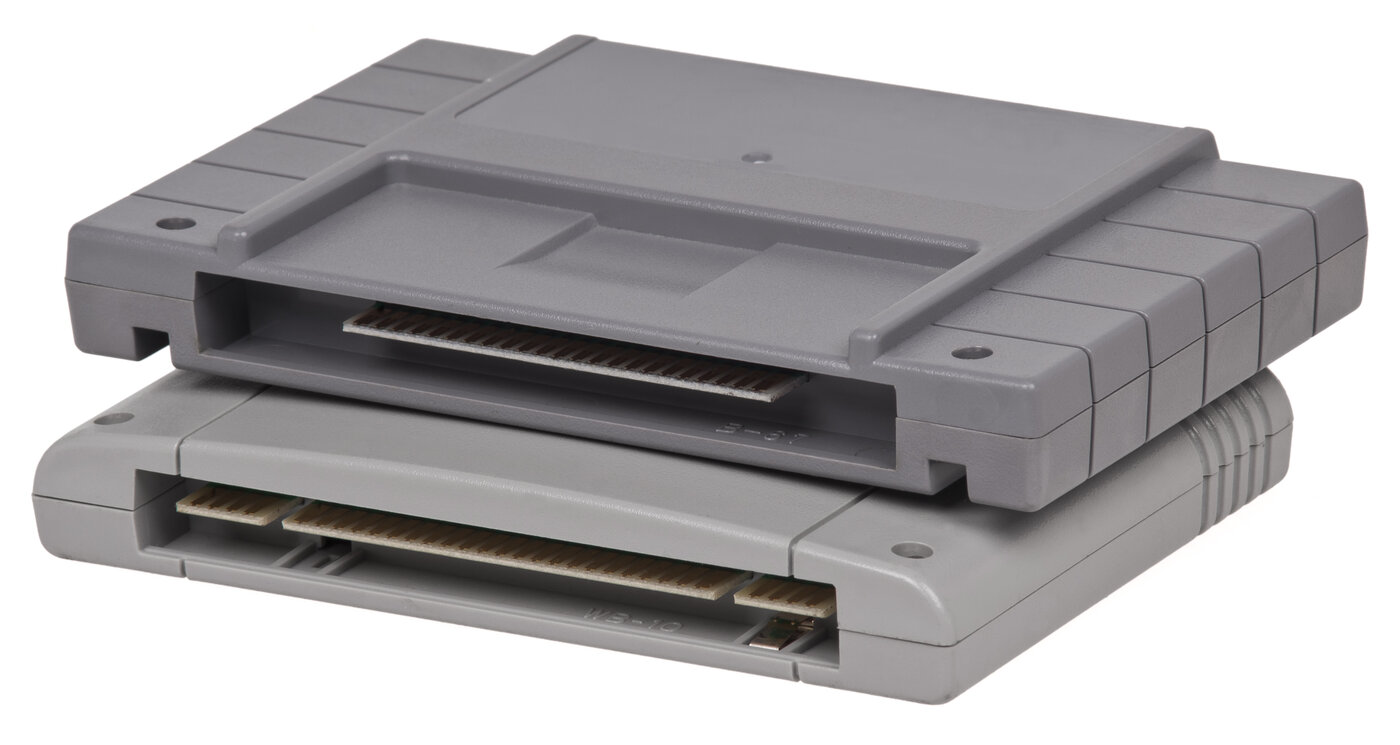A rectangular grey Super NES cartridge above a rounded Super Famicom cartridge, with their moulded shells and connector openings visible.